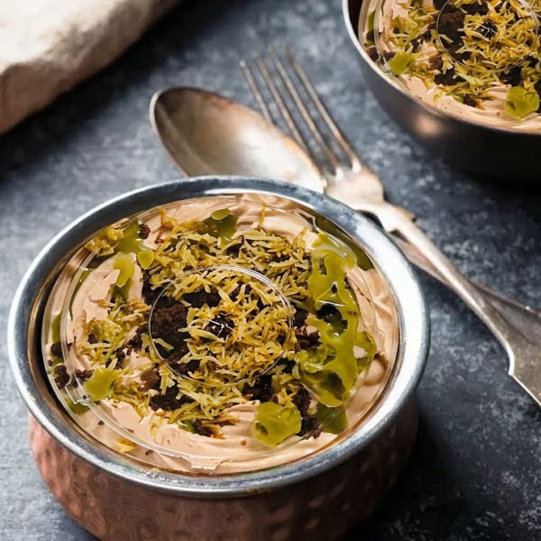Two copper bowls of creamy dessert topped with green drizzle, chocolate crumbles, and shredded coconut.