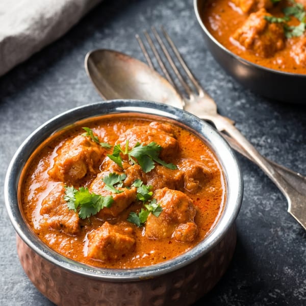 Two copper bowls of chicken tikka masala, garnished with cilantro, on a dark stone surface.